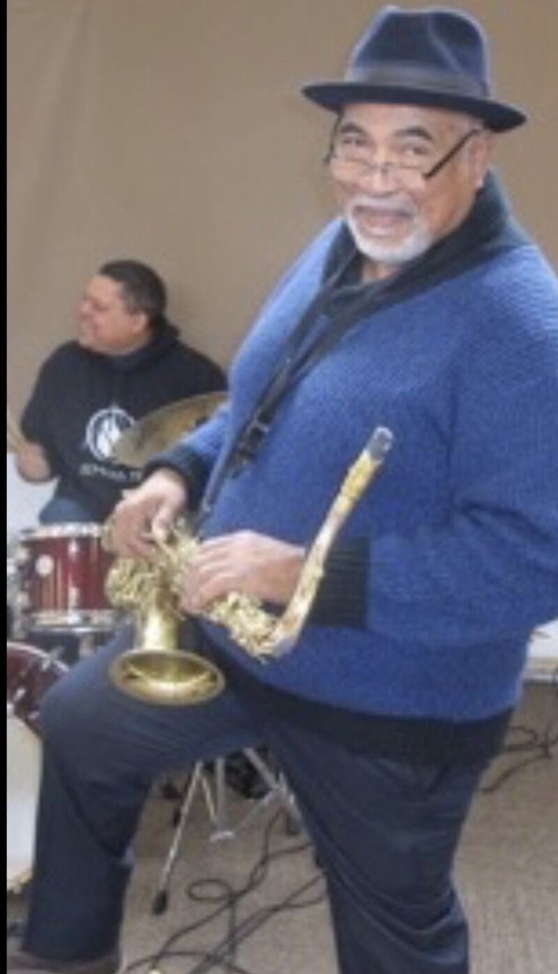 Ron Burris smiling while playing saxophone in a blue sweater